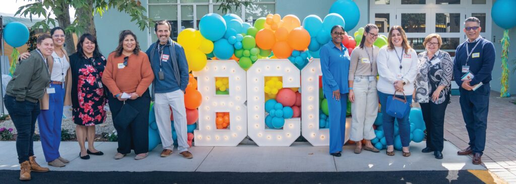 10 BCC staff members stand in front of a display of colorful balloons and large light up letters that spell out "BCC"